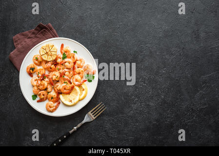 Gamberi arrosto con limone, aglio ed erbe aromatiche. Frutti di mare, shelfish. Gamberi in padella con spezie, aglio e limone su pietra nera di sfondo, copia Foto Stock