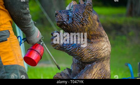 Un uomo una spruzzatura di vernice su un cane scultpure di legno è un grande cane che è scolpita con il grande bosco Foto Stock