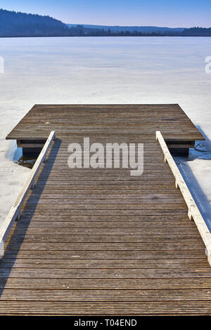 Pontile in legno lungo un lago ghiacciato con un cielo blu Foto Stock