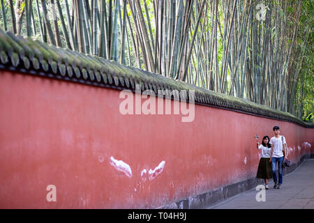 Giovane rendendo selfie a curva pareti rosse passaggio circondato da foreste di bambù, marciapiede con bambù, tempio di Wuhou, Chengdu nella provincia di Sichuan, in Cina Foto Stock
