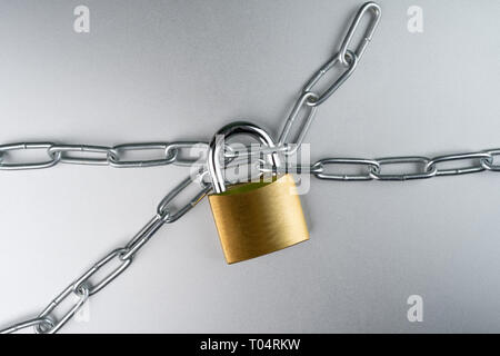 Il lucchetto con catena in acciaio su sfondo grigio. La sicurezza concetto astratto. Foto Stock