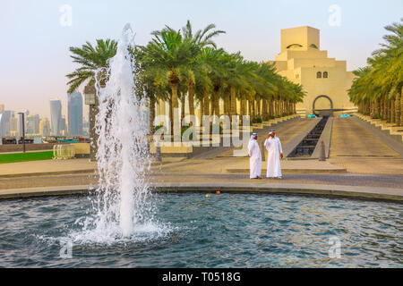 Doha, Qatar - 16 Febbraio 2019: due arabi in piedi vicino alla fontana del Museo di Arte Islamica con grattacieli di West Bay skyline sullo sfondo. Medio Foto Stock