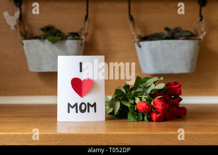 Felice Festa della mamma Festa di compleanno o di sfondo. In casa biglietto di auguri e bouquet di rose rosse sul banco di cucina. Foto Stock