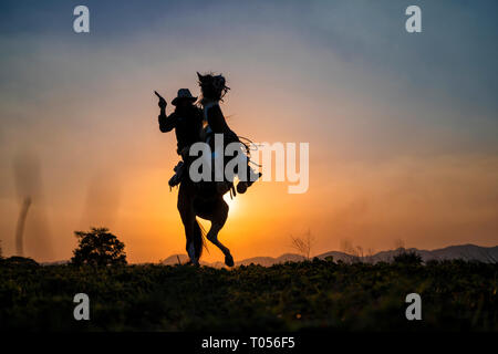 Silhouette cowboy sparare una pistola su un cavallo in sunset Foto Stock