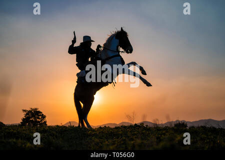 Silhouette cowboy sparare una pistola su un cavallo in sunset Foto Stock