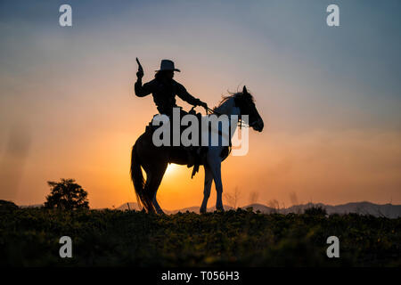 Silhouette cowboy sparare una pistola su un cavallo in sunset Foto Stock