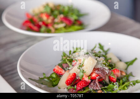 Closeup fresca insalata estiva con basturma traballante, verdi, rucola, fragole, melone e parmigiano. Concetto di delicatezza, nuovo menu nel ristorante alla moda Foto Stock