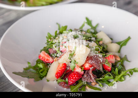 Closeup fresca insalata estiva con basturma traballante, verdi, rucola, fragole, melone e parmigiano. Concetto di delicatezza, nuovo menu nel ristorante alla moda Foto Stock