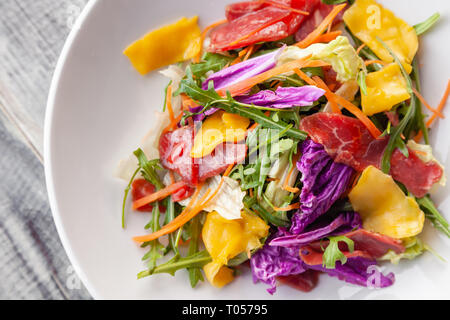 Closeup fresca insalata estiva con bresaola carne, verdi, rucola, mango, la carota e il cavolo cinese. Concetto delicatezza italiano, il nuovo menu in un quartiere alla moda di restaur Foto Stock