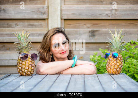 Donna tra due ananas indossando occhiali da sole, come se lei è tra i suoi migliori amici Foto Stock