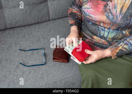 Le mani di un anziano pensionato azienda portafoglio in pelle con valuta polacca denaro. Concetto di sicurezza finanziaria nella vecchiaia. Foto Stock