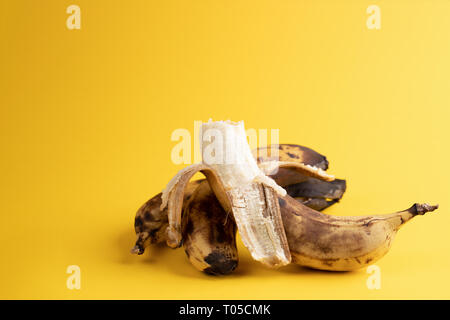 Una banana pelati e non pelati due surmature annerite brutto banane sul colore giallo brillante background. Foto Stock