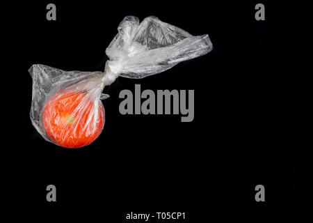 Un pomodoro rosso trasparente in busta di plastica chiusa su sfondo nero. Foto Stock