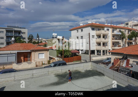 Limassol, Cipro - 4 Novembre 2018: l'uomo in piedi nel centro di recente cantiere livellato tenendo un tubo flessibile e la spruzzatura di acqua sulla ghiaia prima di fl Foto Stock