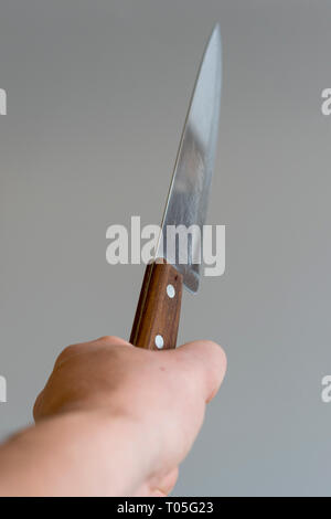 Mano d'uomo con un coltello su sfondo grigio. Concetto di violenza. La mano di un gangster con un coltello. foto verticale. Foto Stock