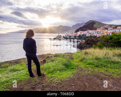 Giovane uomo alla ricerca di una vista di conico, una città nell'isola di Madeira, Portogallo, al tramonto. Foto Stock