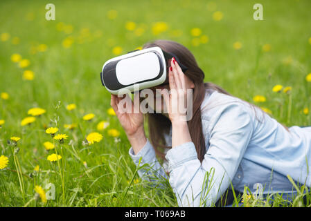 Donna che utilizza la realtà virtuale auricolare posa all'aperto nella primavera di campo dei fiori Foto Stock