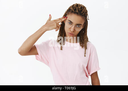 Vita-up shot di esaurito e briga elegante attraente ragazza con la pelle scura e dreadlocks compiendo il gesto della pistola vicino tempio essendo infastiditi e Foto Stock