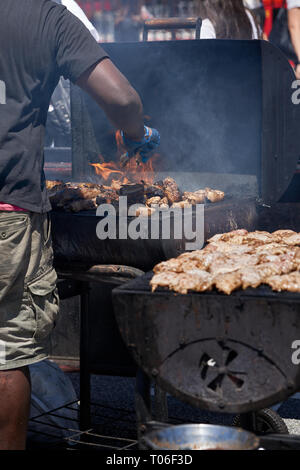 Un uomo manning una fiamma di un barbecue per la cottura della carne. Foto Stock