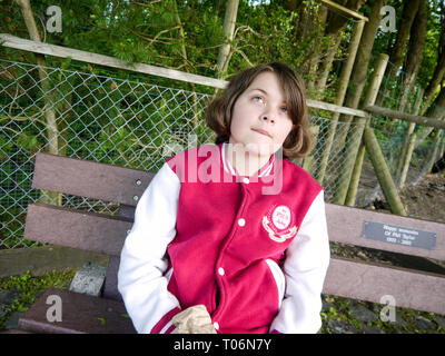 Giovane ragazza seduta su una panchina pensando all'aperto / chiedendo / ponderando Foto Stock