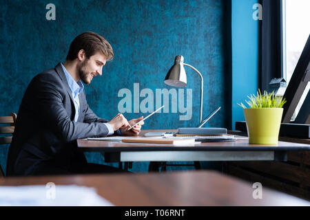 Uomo sorridente in ufficio a lavorare sulla tavoletta digitale. Foto Stock
