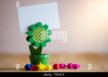 Clip di supporto supporto carta verde a forma di girasole e multicolore di stelle di carta su un tavolo di legno. In plastica bianca scheda vuota nella luce del sole di mattina. Foto Stock