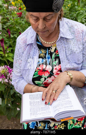 I vecchi donna ebrea indossare gioielli legge il suo libro di preghiere nel giardino sul retro. Foto Stock
