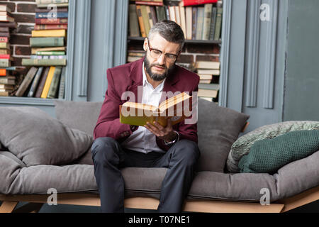 Imprenditore barbuto sentirsi coinvolti nella lettura di libro che parla di denaro Foto Stock