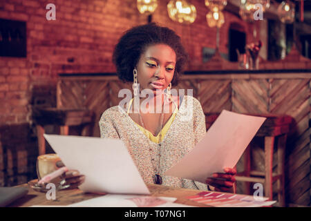 Attraente afro-designer americano controllo schizzi mentre trascorrere tempo nella caffetteria. Foto Stock