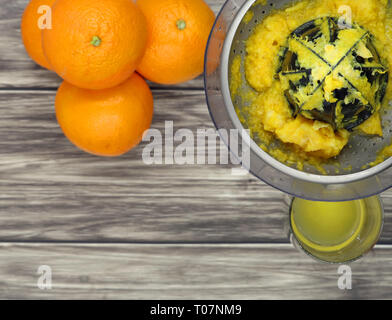 Vista dall'alto di arance, un distributore di succo di frutta e un bicchiere di succo di frutta su sfondo di legno, spazio di copia Foto Stock