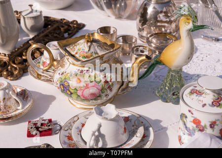 Dettaglio del vetro bird e vintage tè pentola tra Cina tazze in vendita al mercato di strada, girato in condizioni di intensa luce invernale a Cremona, Lombardia, Italia Foto Stock