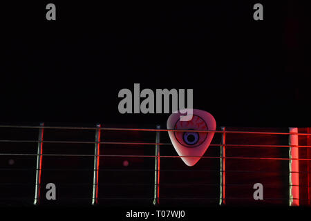 Chitarra elettrica al collo con un fresco guitar pick illuminato con luce rossa in uno sfondo scuro (foto è liscia e non disturbato come sembra in anteprima) Foto Stock