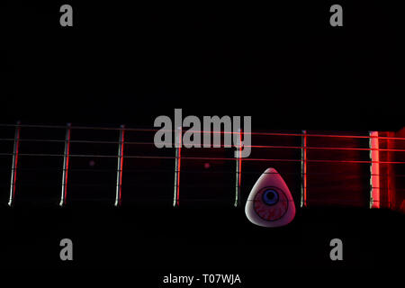 Chitarra elettrica con collo cool guitar pick illuminato con luce rossa in uno sfondo scuro (foto è liscia e non disturbato come sembra in anteprima) Foto Stock