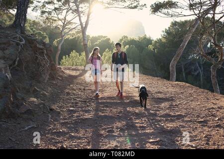 Fratello e Sorella di escursionismo con il cane di famiglia nella foresta al tramonto Foto Stock