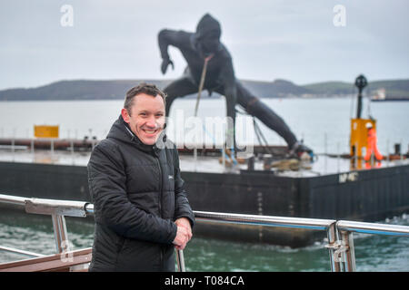 L'artista Giuseppe Hillier su una barca accanto alla sua scultura, Messenger, il più grande in fusione di bronzo scultura NEL REGNO UNITO, come si arriva a Plymouth Sound da includersi come si fa il suo modo di essere installato al di fuori Theatre Royal Plymouth, Devon. Foto Stock