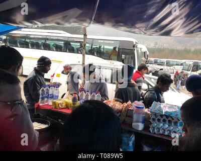 MANALI, HIMACHAL PRADESH—2018 MARZO: I passeggeri in attesa dei loro autobus si rifugiano dalla pioggia in una tenda presso il terminal degli autobus pubblici di Manali. Foto Stock