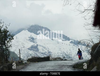 MANALI, HIMACHAL PRADESH--MARZO 2018: Vista delle montagne innevate nelle catene montuose dell'Himalaya con una donna che cammina sulla strada. Foto Stock