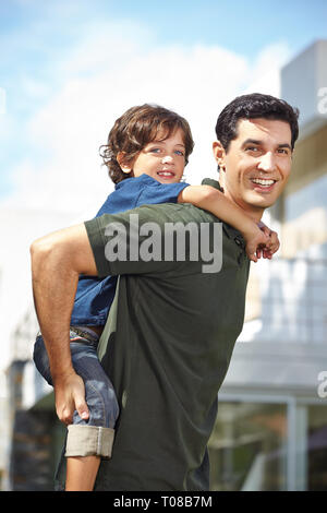 Padre porta il suo figlio piggyback sulla sua schiena in giardino Foto Stock