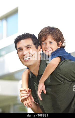 Padre Felice porta il suo piccolo figlio di piggyback sulla sua schiena Foto Stock