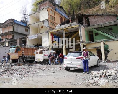 KULLU, HIMACHAL PRADESH, INDIA - MARZO 2018: Le persone si siedono all'esterno di edifici in fase di ristrutturazione da parte della strada nel distretto di Kullu. Foto Stock