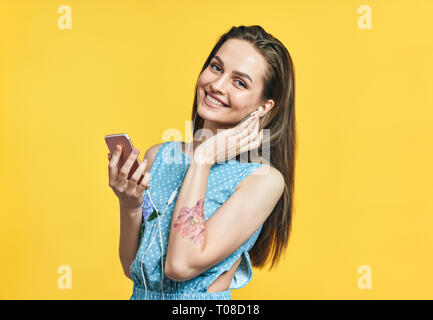 Bella giovane donna in cuffie e smart phone ascoltando musica su sfondo giallo Foto Stock