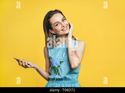 Bella giovane donna in cuffie e smart phone ascoltando musica su sfondo giallo Foto Stock