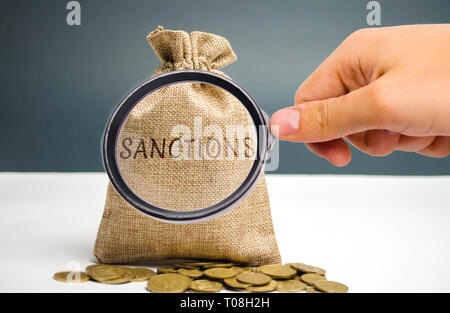 Una lente di ingrandimento è guardando un sacco di denaro con la parola sanzioni. L'istituzione del Comitato economico e sanzioni politiche sui temi di geopolitic Foto Stock
