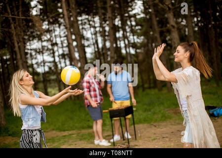 Giovani donne giocando a pallavolo su picnik in primavera la natura mentre gli uomini preparare grill Foto Stock