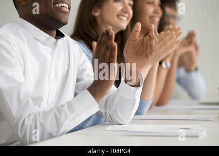 Multirazziale pubblico business la gente applaude seduti al tavolo da conferenza, primo piano Foto Stock