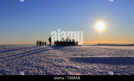 Le persone che si godono il sole invernale sulla cima del monte Brocken, la vetta più alta delle montagne Harz. La coperta di neve pietra del vertice prima del tramonto. Foto Stock
