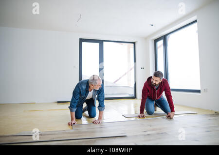 Un uomo maturo con il suo anziano padre la posa di pavimenti in legno, un nuovo concetto di casa. Foto Stock