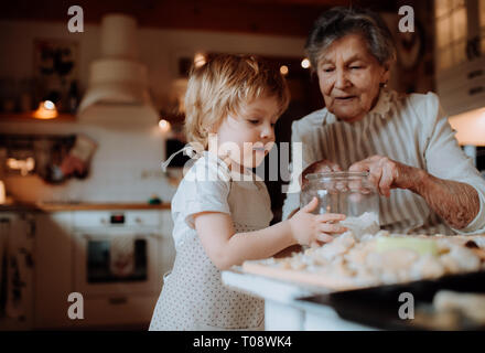 Nonna senior con piccole toddler boy fare torte a casa. Foto Stock