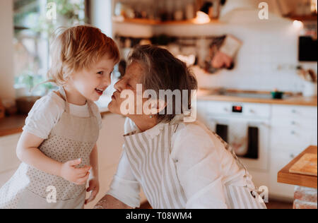 Nonna senior con piccole toddler boy fare torte a casa, baciare. Foto Stock