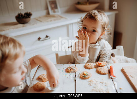 Due bimbi piccoli bambini seduti al tavolo, decorare e mangiare dolci di casa. Foto Stock